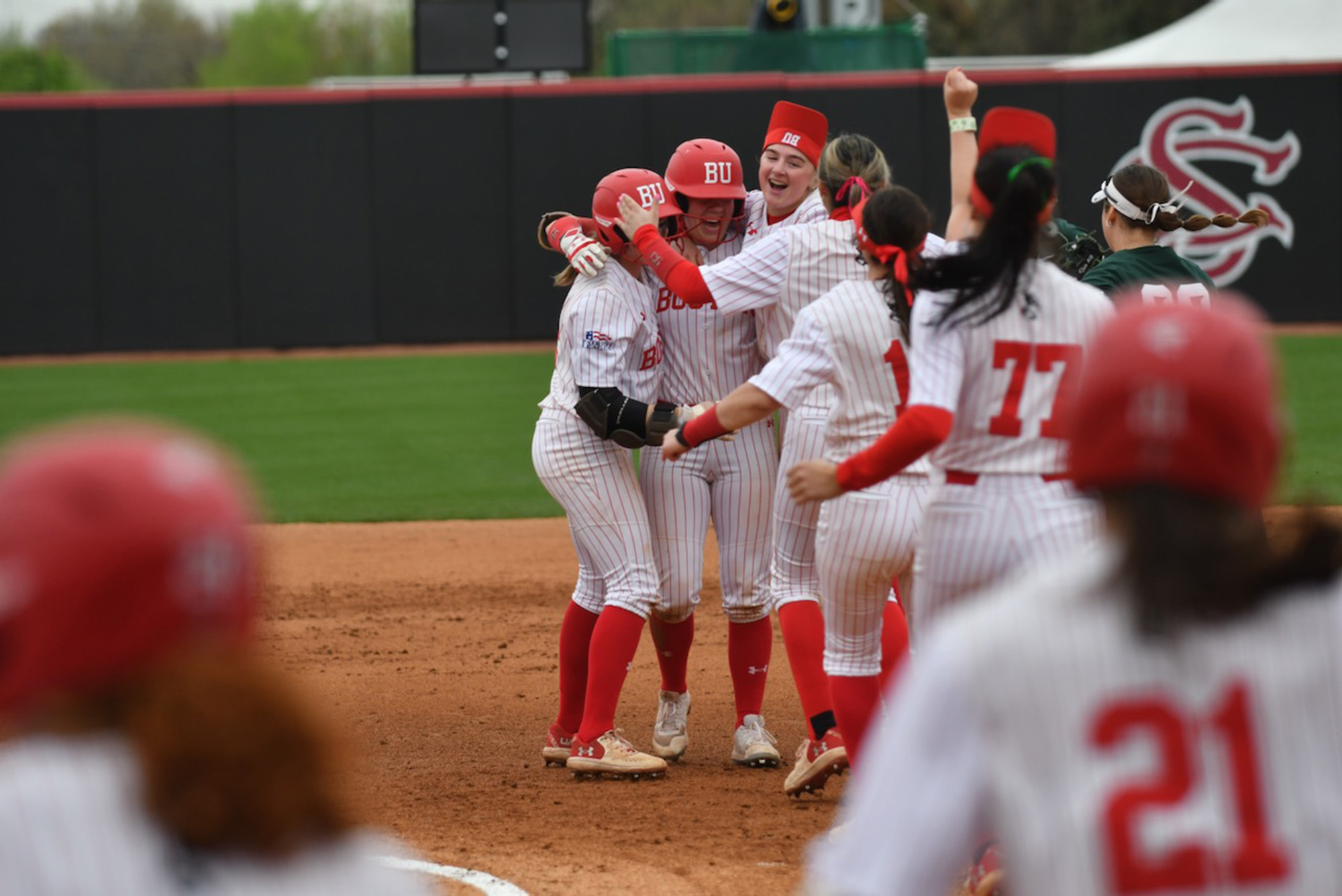 Photo: A softball team celebrating. They are wearing white uniforms with red accents