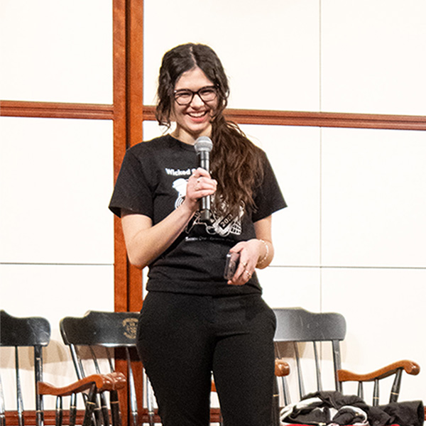 Photo: A college student wearing glasses and holding a microphone introduces a sketch at a recent comedy show on BU's campus