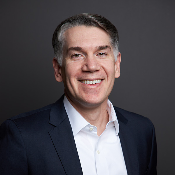 Photo: A man with short hair and a smile wearing an elegant dark suit and white collared shirt