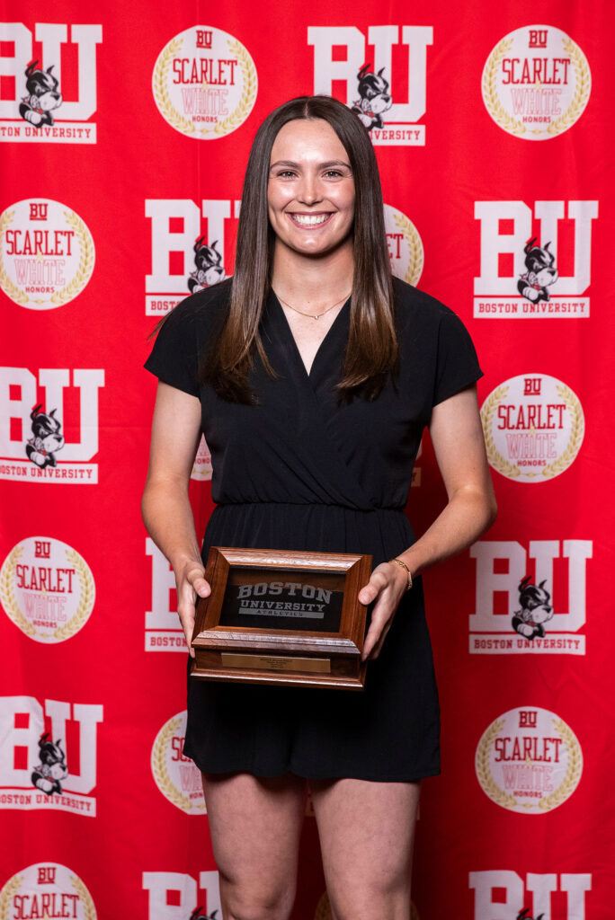 Photo: A picture of a woman in a black dress posing with a plaque. There is a red background that says "BU" behind her