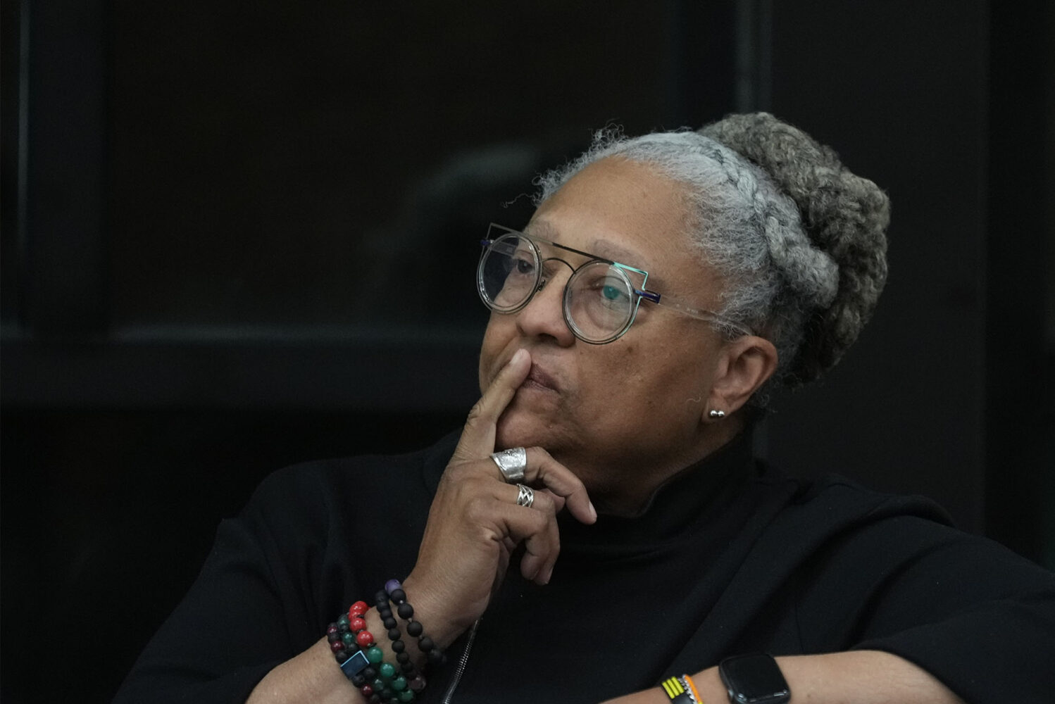 Photo: A black woman wearing multiple bracelets sits with a pensive and serious expression in this portrait in front of a black background