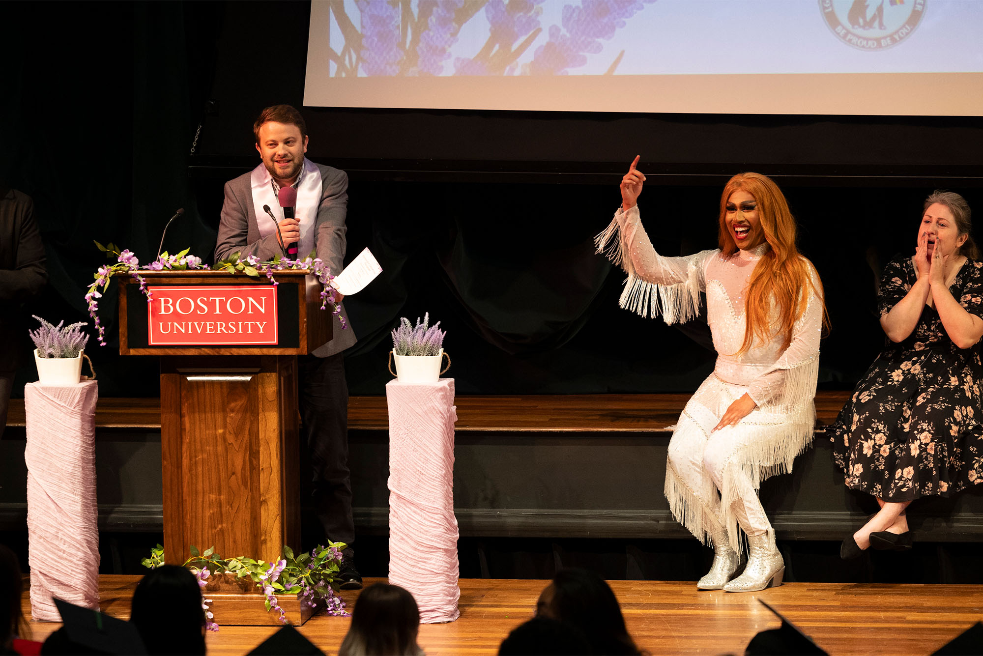 Photo: A man stands at a podium alongside two women on the stage to the right at a recent ceremony during Boston University's commencement in 2024