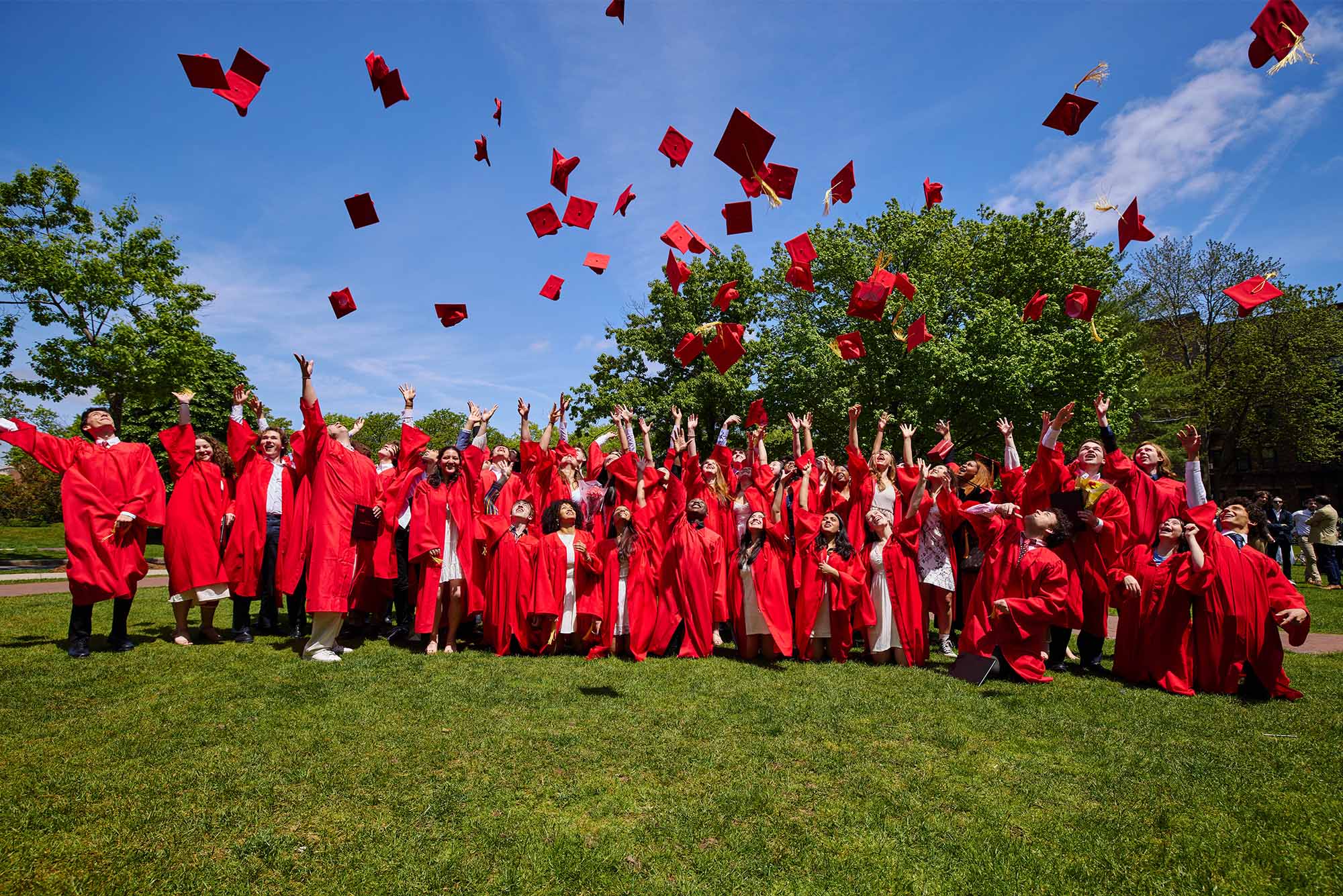 Photo: A sea of graduates in red gowns throw their caps into the air at the Boston University Academy Commencement in 2024