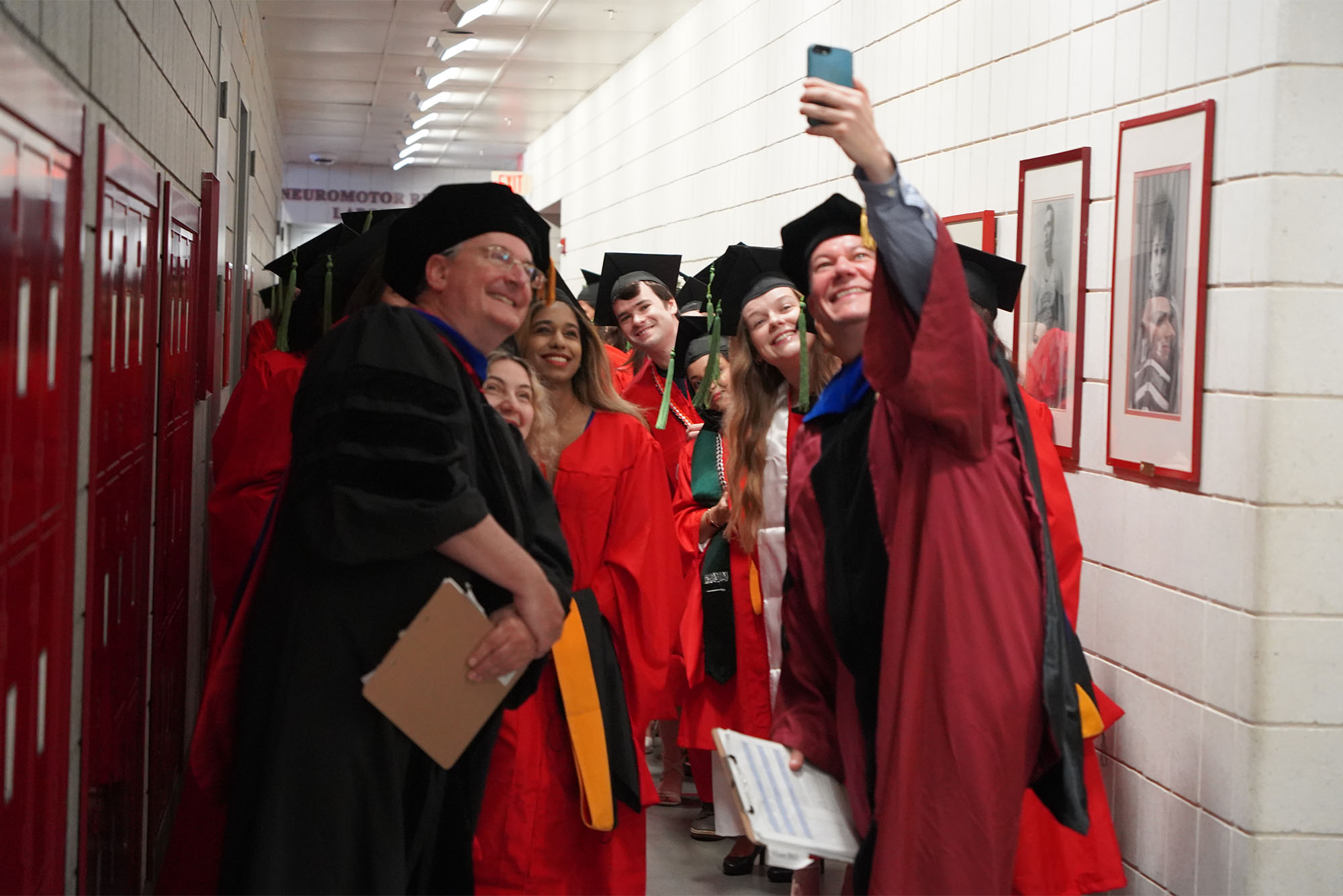 Photo: Louis Toth, a Chobanian & Avedisian School of Medicine associate clinical professor of anatomy and neurobiology, and Adam Hall, an assistant professor of anatomy and neurobiology, with Graduate Medical Sciences students at their May 16 convocation ceremony. A group of graduating students in robes snap a selfie with each other prior to the ceremony.
