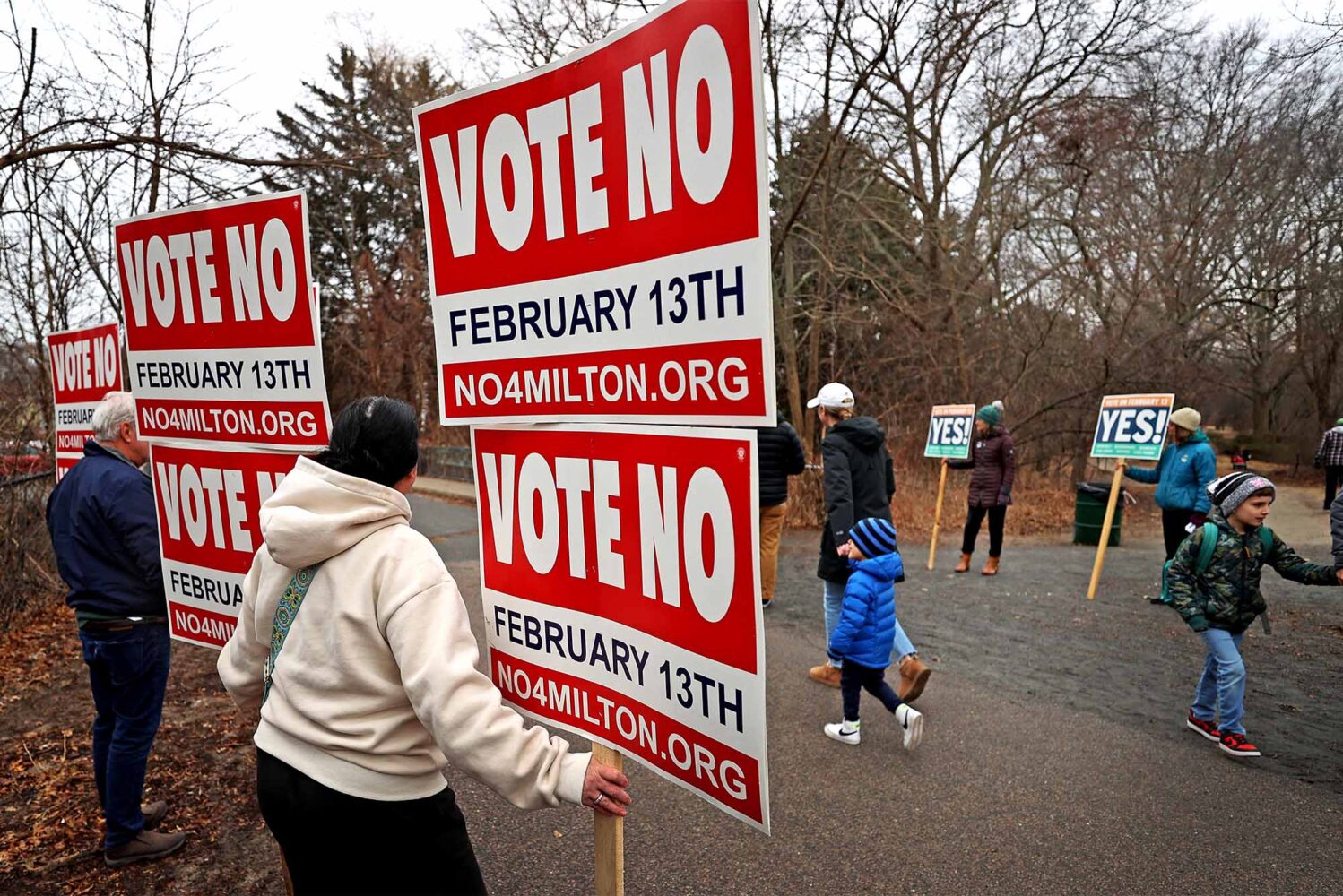 Photo: Demonstrators with signs reading "Vote No February 13th" advocating against a new MBTA transit law implemented by the state of Massachusetts. Vote Yes signs can be seen in the distance.
