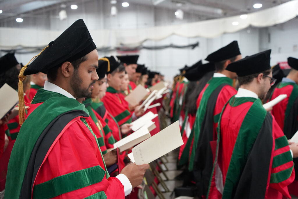 Photo: Newly minted doctors wearing red robes and doctoral hoods recite the Hippocratic Oath at the conclusion of the Chobanian & Avedisian School of Medicine’s MD and PhD convocation ceremony May 16 at the BU Track & Tennis Center
