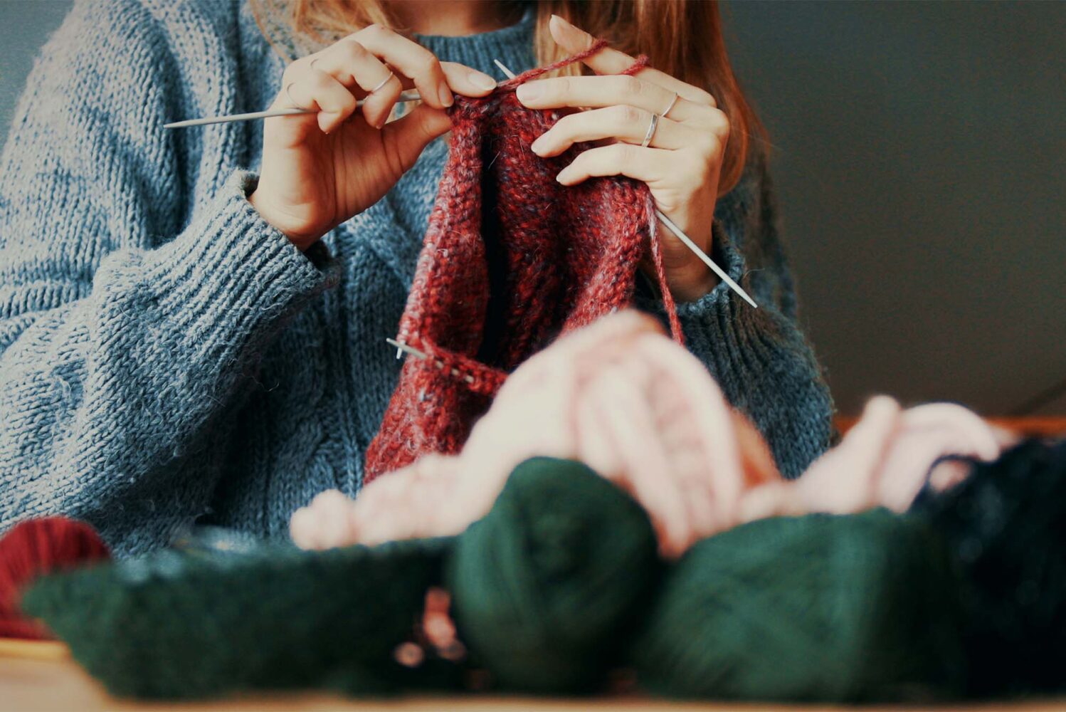 Photo: A young woman knitting with balls of yarn on the table in front of her, in various colors