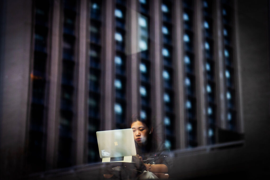 Photo: A picture of a reflection of a building with someone working on their laptop