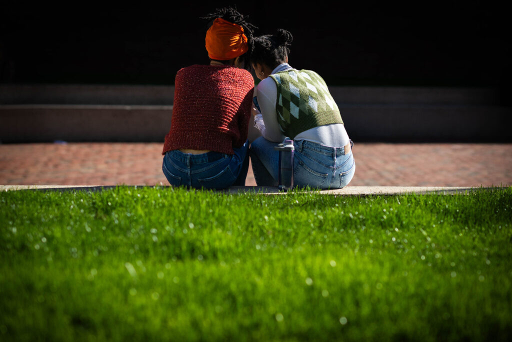 Photo: A picture of the back of two people leaning into one another as they sit on green grass