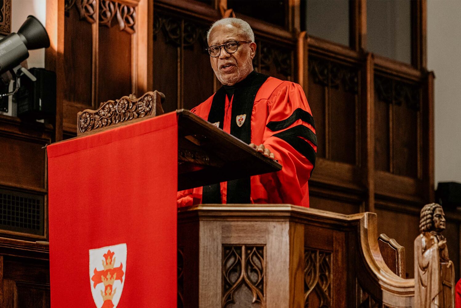 Photo: A man in a red gown gives a speech at a podium draped in a red covering. Baccalaureate speaker Walter E. Fluker (GRS’88, STH’88) told Boston University’s Class of 2024 graduates Sunday to follow the example of BU’s most famous alumnus, Martin Luther King, Jr., in striving for peace and justice. Photo by Kelly Davidson