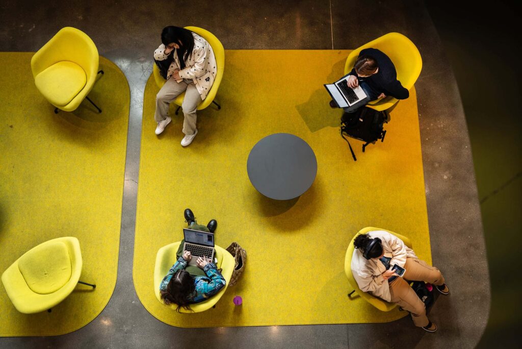 Photo: A picture of a space with yellow chairs and yellow rugs where people are working