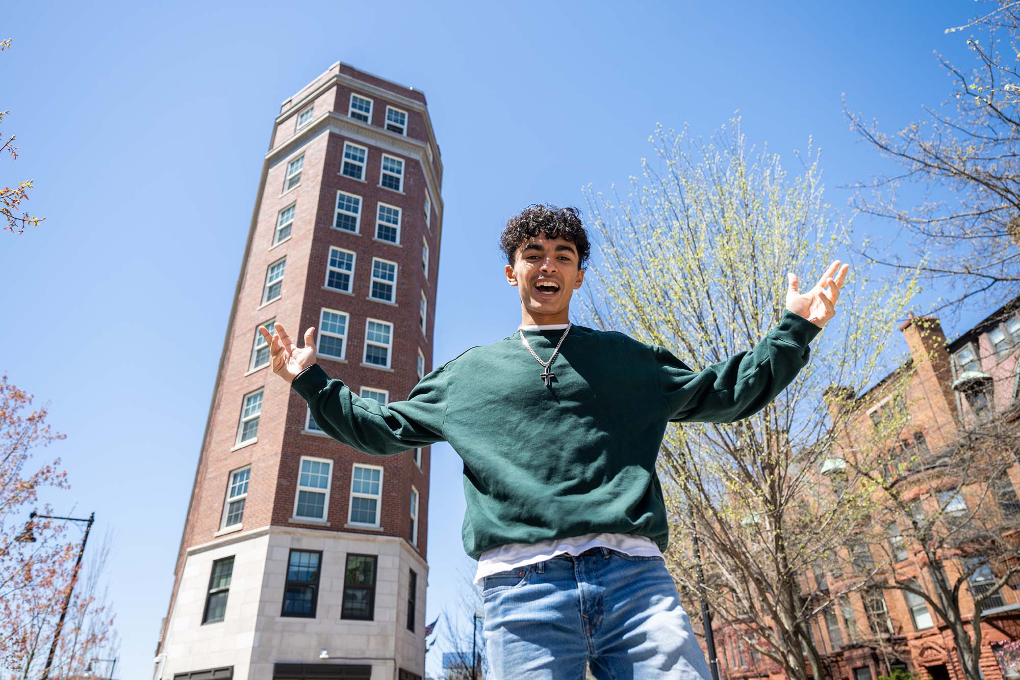 Photo: A picture of a male student posing in front of a dorm building in the city with his arms extended.