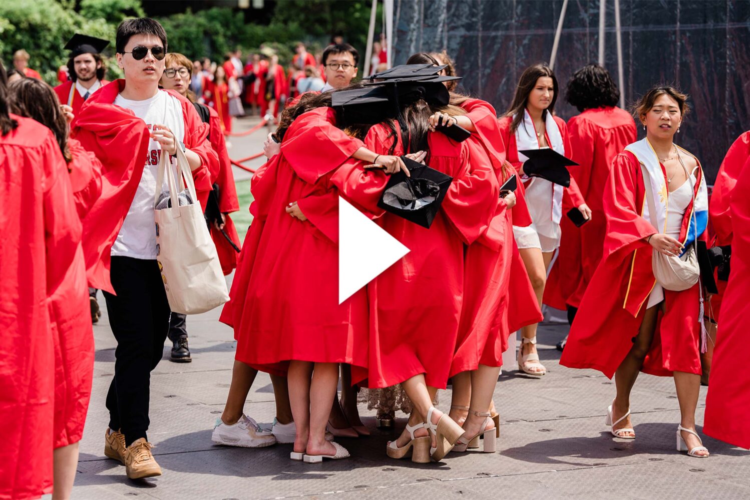 Photo: A picture of people in black graduation caps and red graduation gowns hugging in a crowd