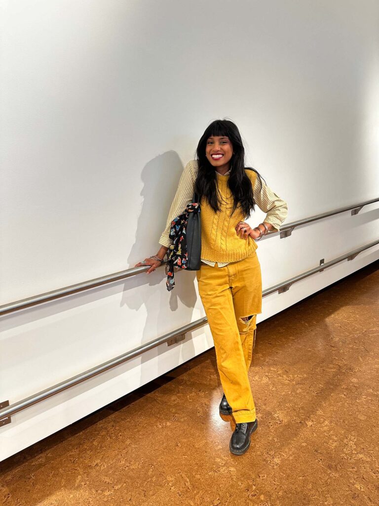 Photo: A picture of a girl with long, dark hair wearing a yellow vest with a yellow button-up top under it. She is wearing yellow pants that match the vest and Dr. Marten boots