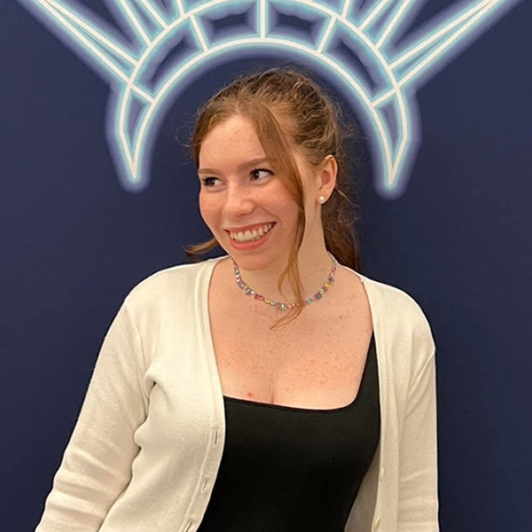 Photo: a woman in a business casual outfit smiles underneath a crown drawn on the wall behind her.