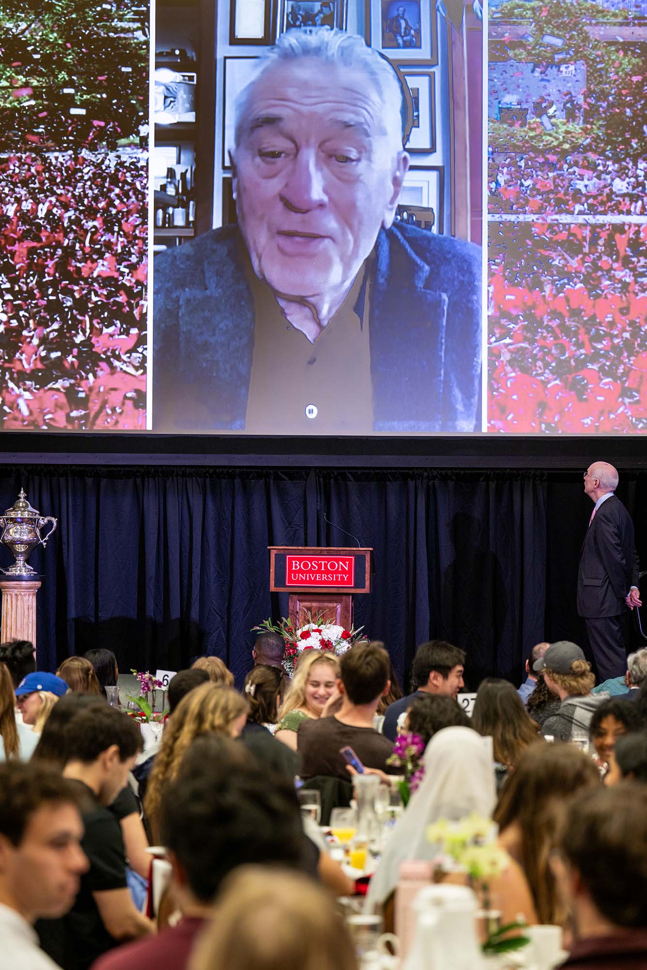 Photo: A picture of a crowd watching a video of Robert De Niro on a projector screen
