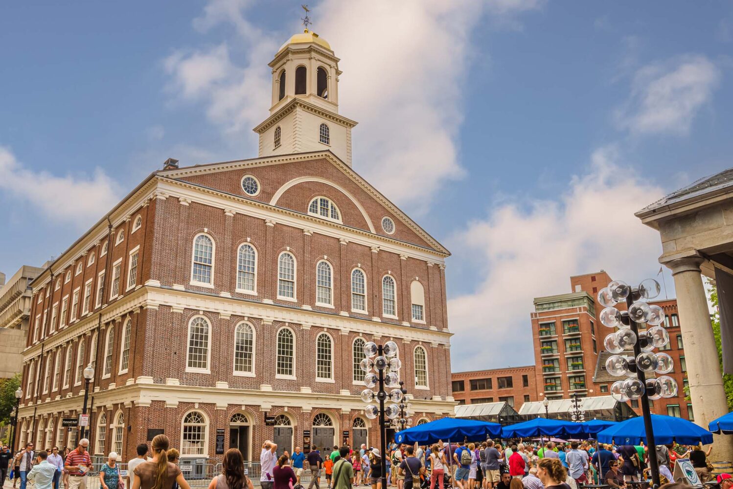 Photo: A picture of the exterior of Faneuil Hall. There are tents and many people walking outside