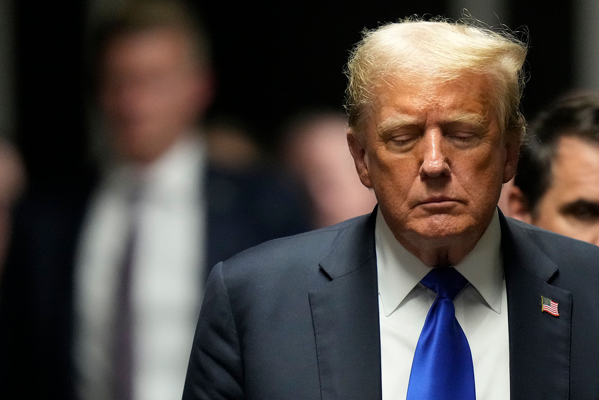 Photo: Donald Trump, an aging man in a blue suit, walks out of a court room with a somber look on his face
