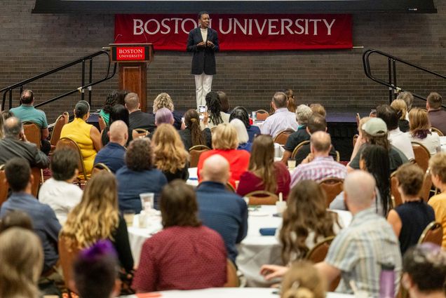 Photo: A picture of BU President Melissa Gilliam onstage in front of many people. There is a banner that says "Boston University" behind her