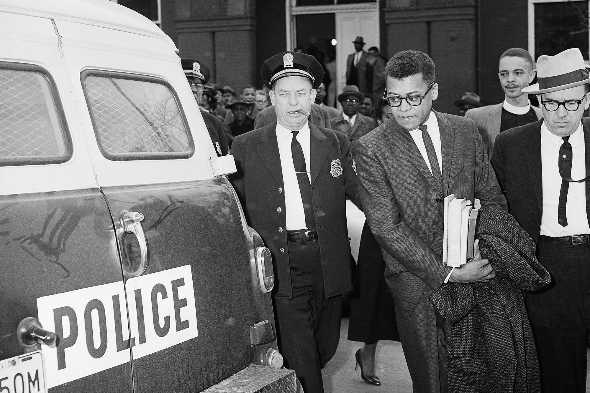 Photo: A picture of a man carrying books being led to a police car by two cops