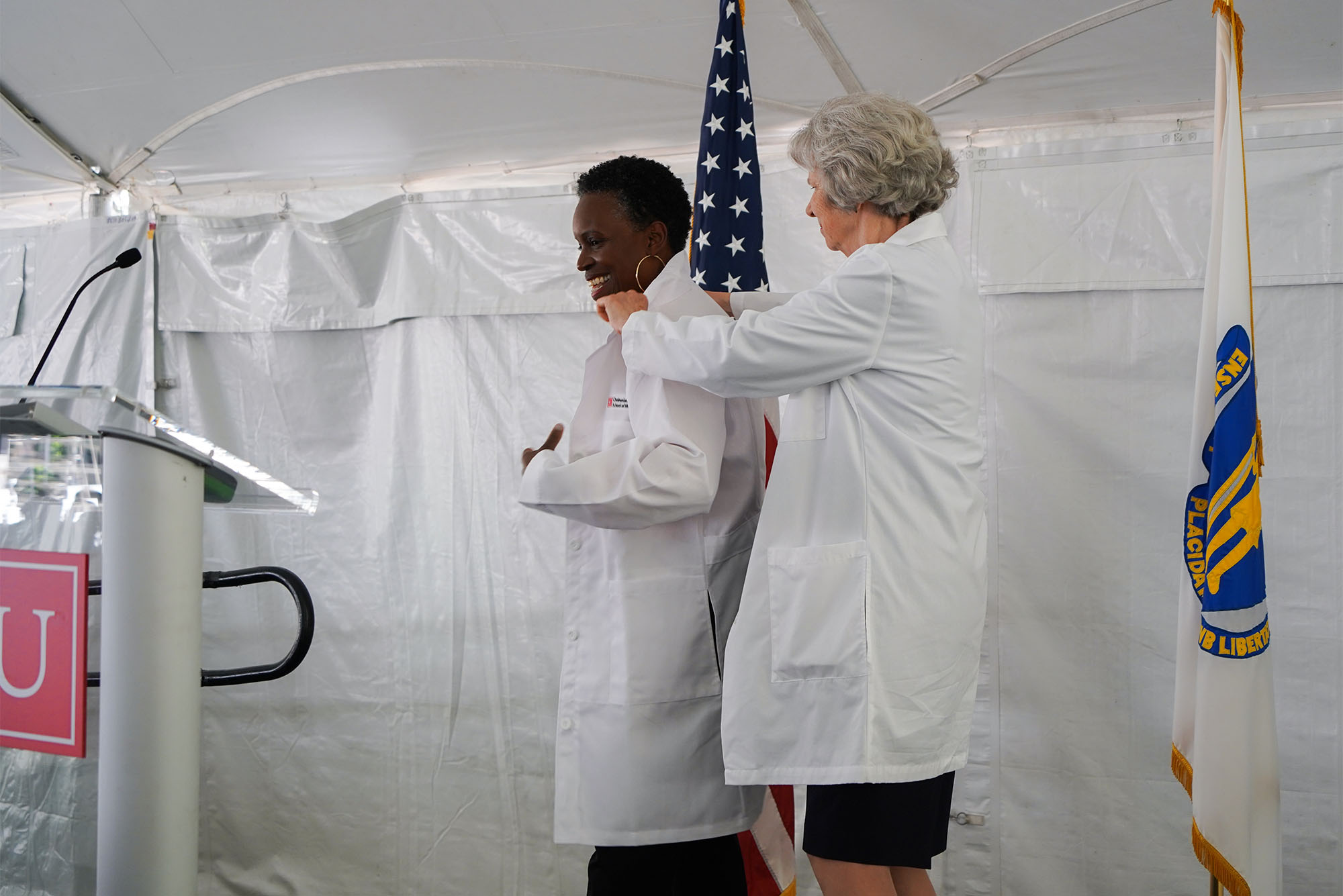 Photo: Karen Antman, dean of the medical school and provost of the Medical Campus (right), helping BU President Melissa L. Gilliam into a white coat at the August 5 White Coat Ceremony. Gilliam was the keynote speaker at the event, which signifies the beginning of medical students’ journeys into the study and practice of medicine. Photo by Jake Mackey