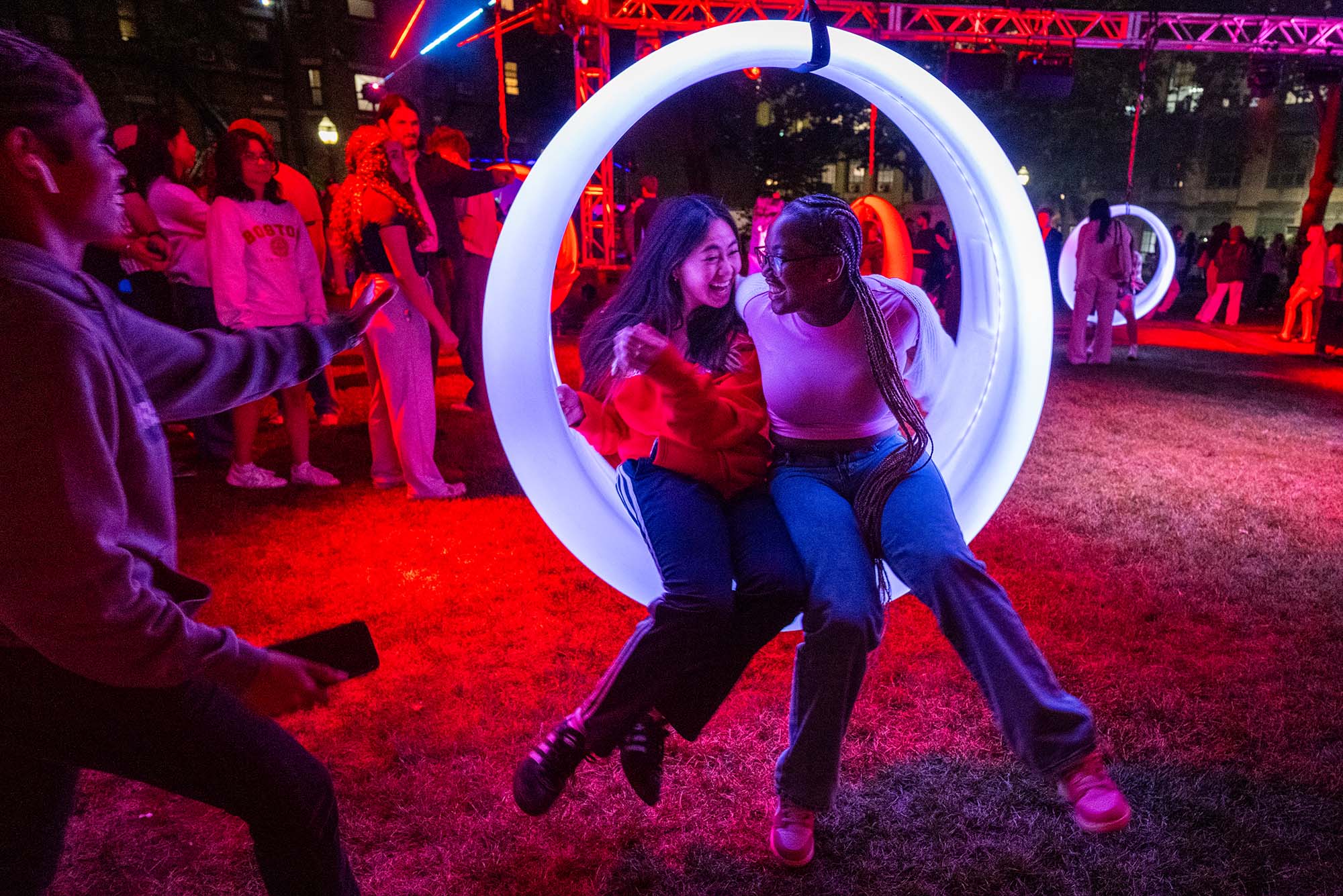 Photo: Two students sitting on a light swing at nighttime during Boston University's Night of Lights.