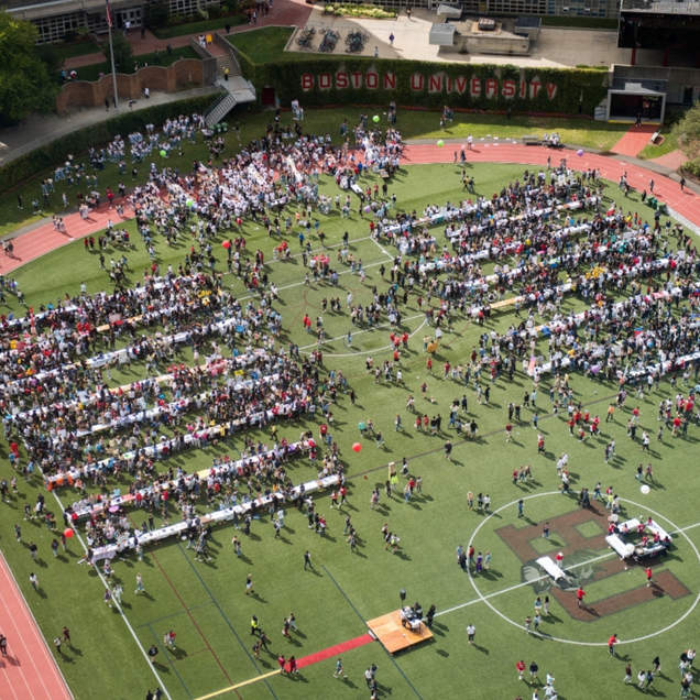 Photo: A large group of hundreds of college students gather on a sports field on a sunny day