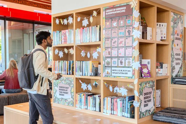 Photo: Amit Yadav, a young man with a white jacket and gray pants, checks out the Howard Thurman Center’s new Lending Library