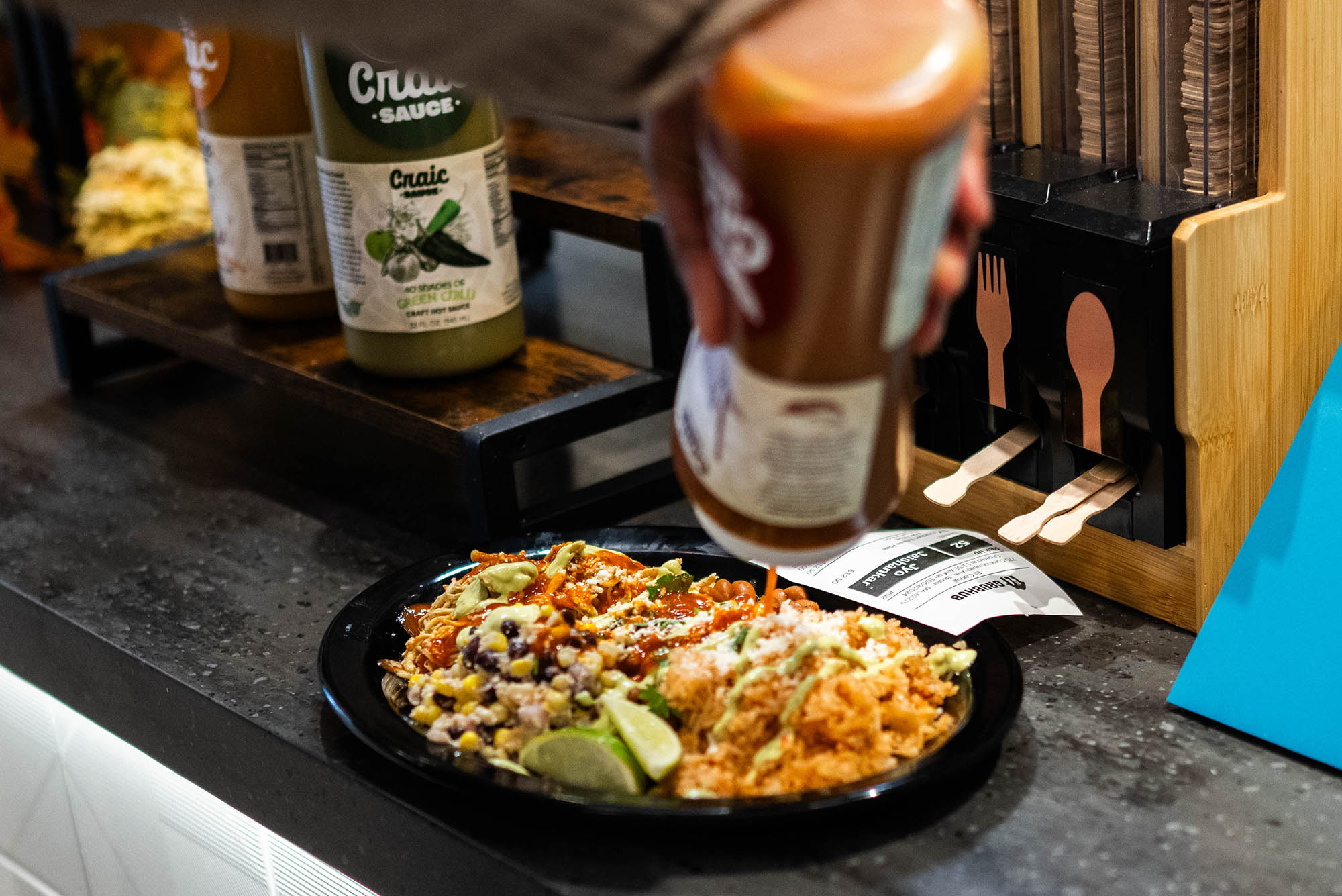 Photo: Someone holding a sauce bottle pours the contents on their plate of food.