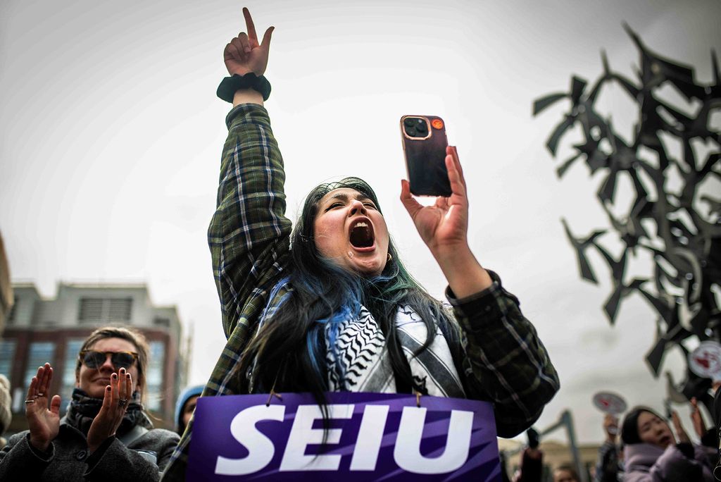 Photo: A woman at a protest with her arm raised and her phone filming