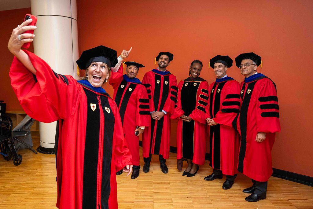 Photo: A group of people in red academic robes with black and blue trim and black caps posing for a selfie