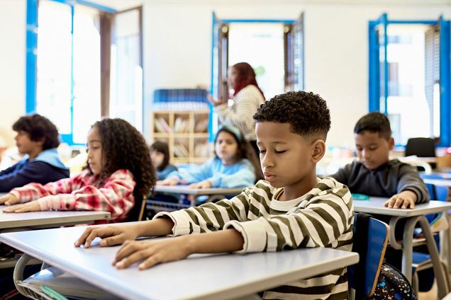 Photo: Waist-up view of young boys and girls sitting at child-size desks with eyes closed and arms relaxed during quiet time.