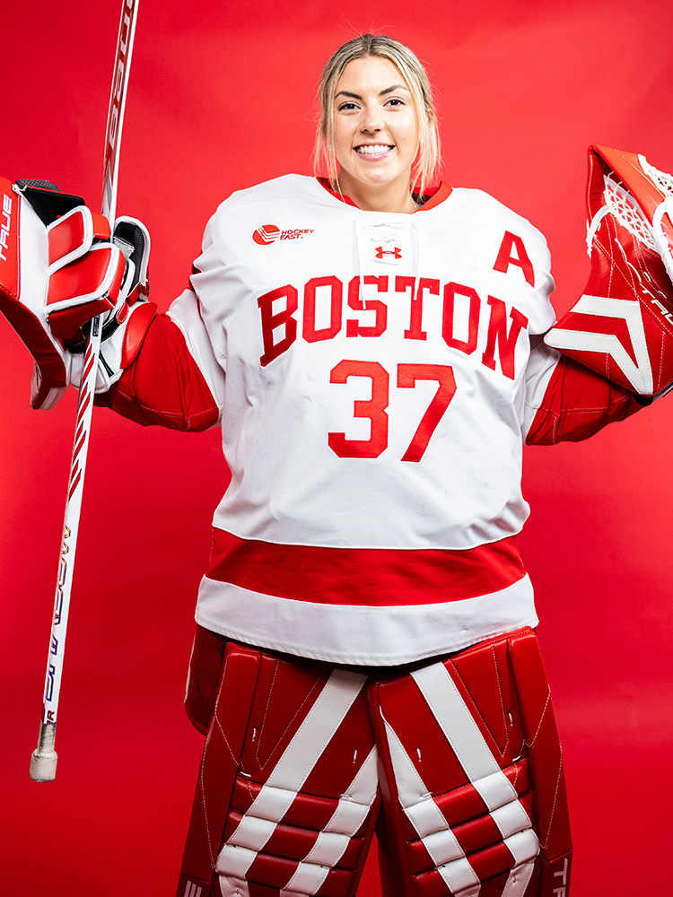 Photo: BU Women's hockey Goaltender Callie Shanahan poses for a headshot in full gear in front of a red background