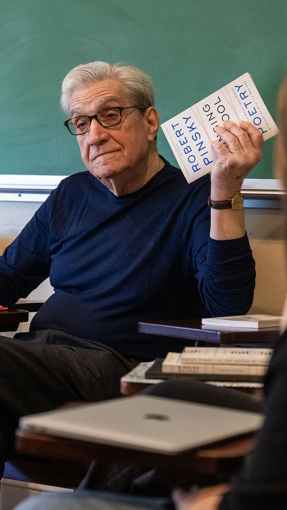 Photo: Robert Pinsky holding up a book of his own poetry in a classroom of students