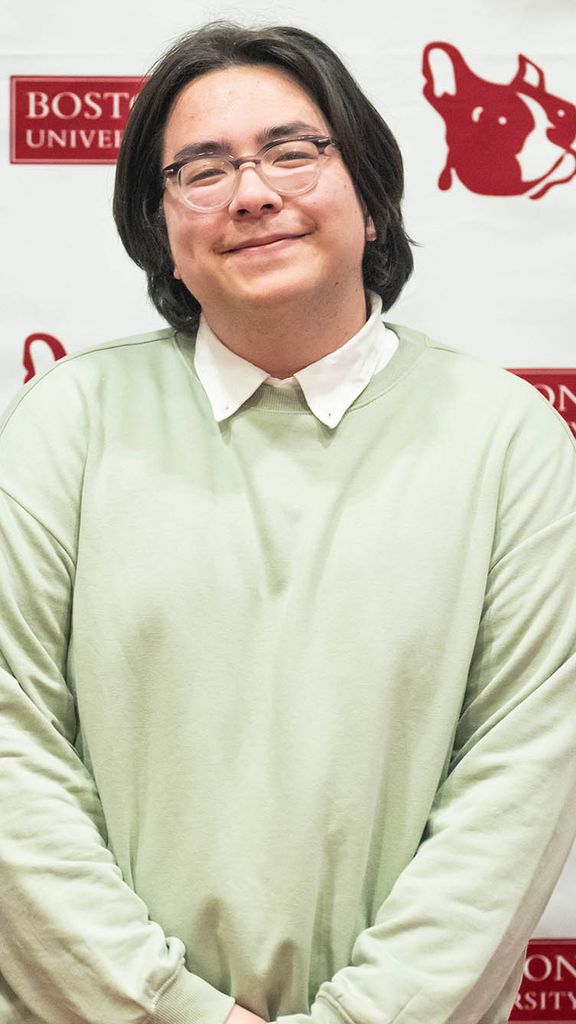 Photo: A young man with chin length black hair poses for a photo in a green sweater.