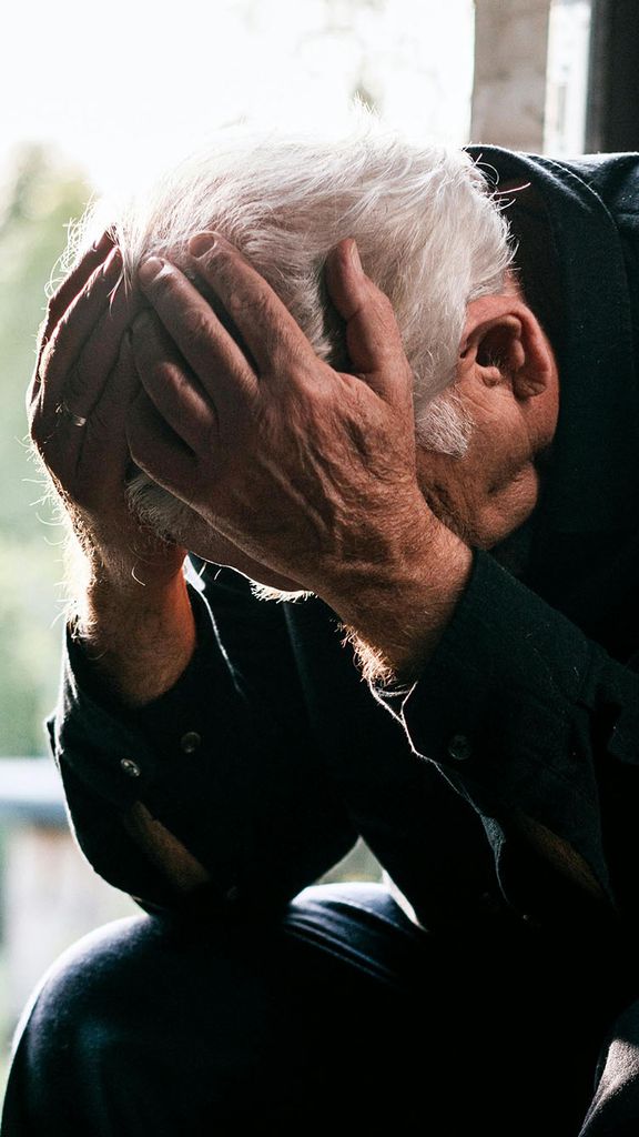Photo: An older man with white hair and his head in his hands