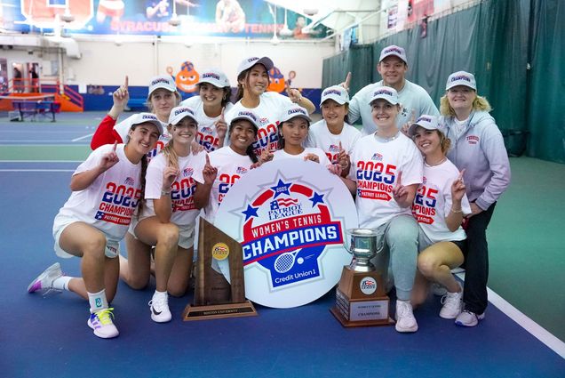 Photo: A group of women in white tennis gear smile and pose around a trophy and a sign claiming their championship.