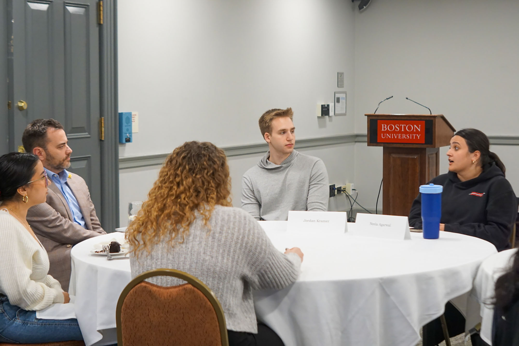Photo: A group of individuals, mainly students, sit around a white clothed round table.