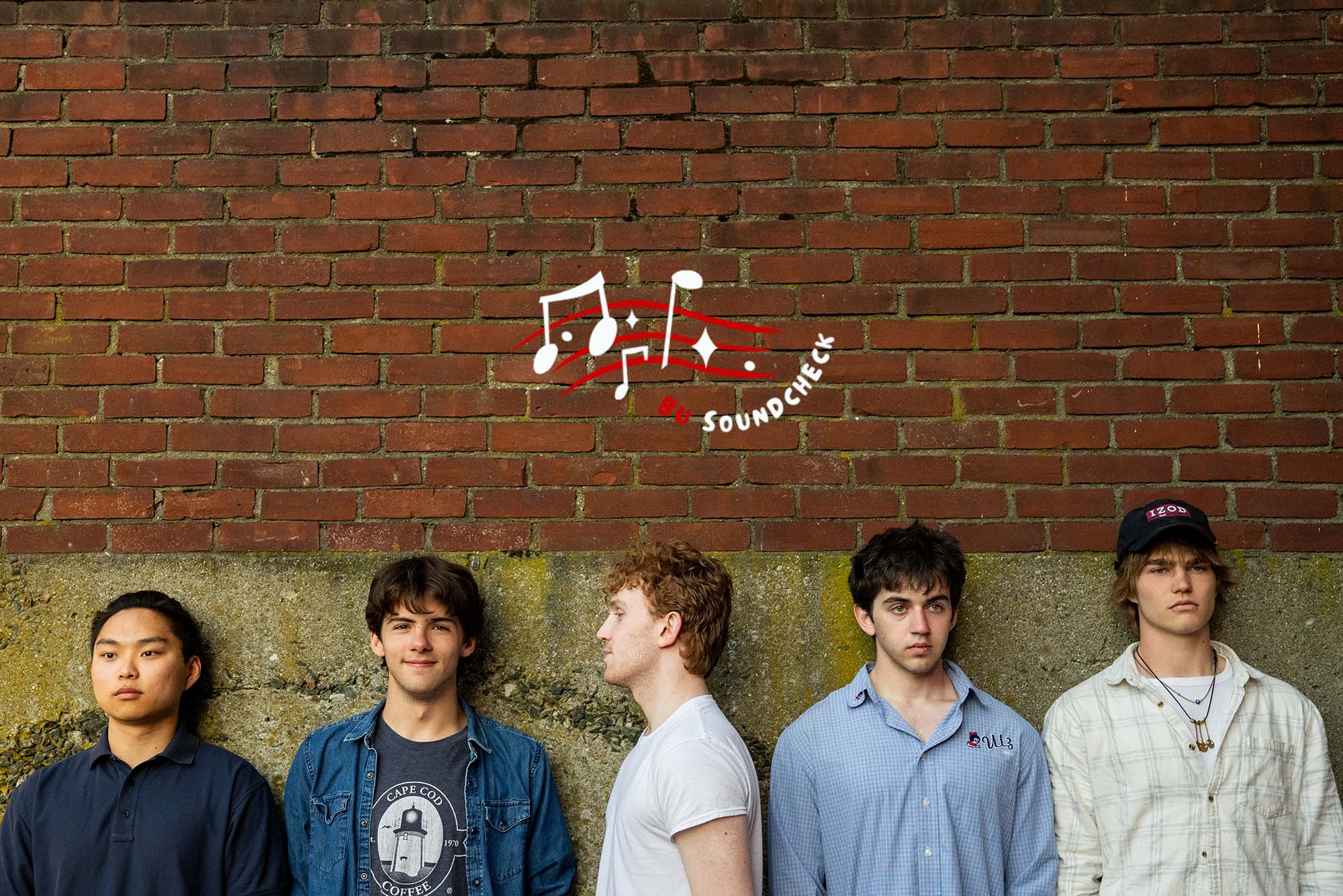 Photo: A band of 5 male members lined up and posing in front of a brick wall. There is a logo over the image that says "BU Soundcheck" in red and white colors with music notes