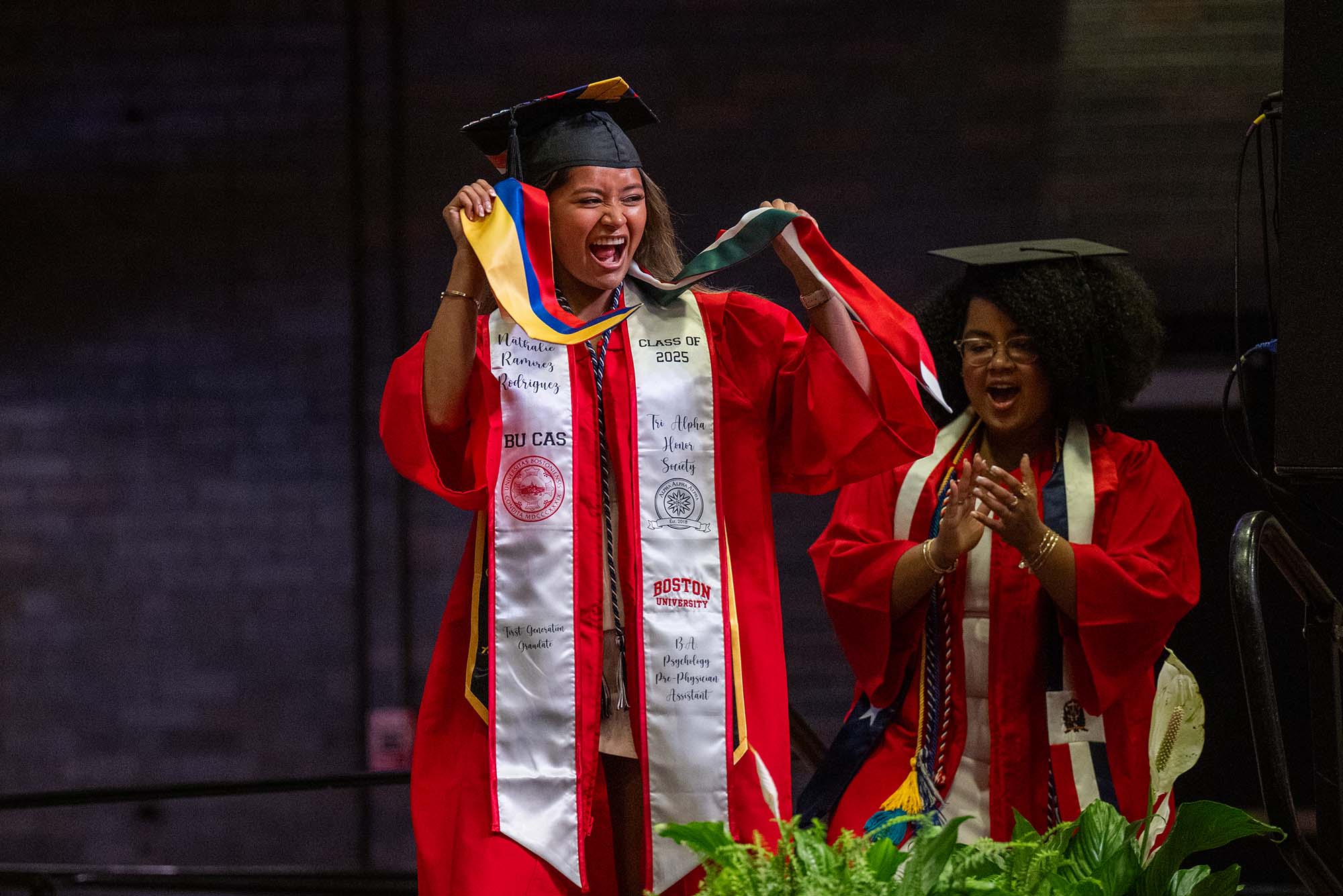 Photo: A female BU student walking across a stage as she receives a Luz y Exito serape