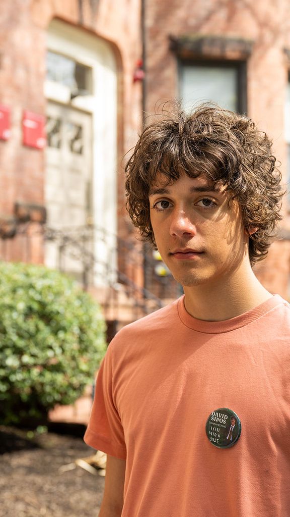 Photo: A male BU studentwith curly brown hair posing in a peach-colored shirt in front of a BU building