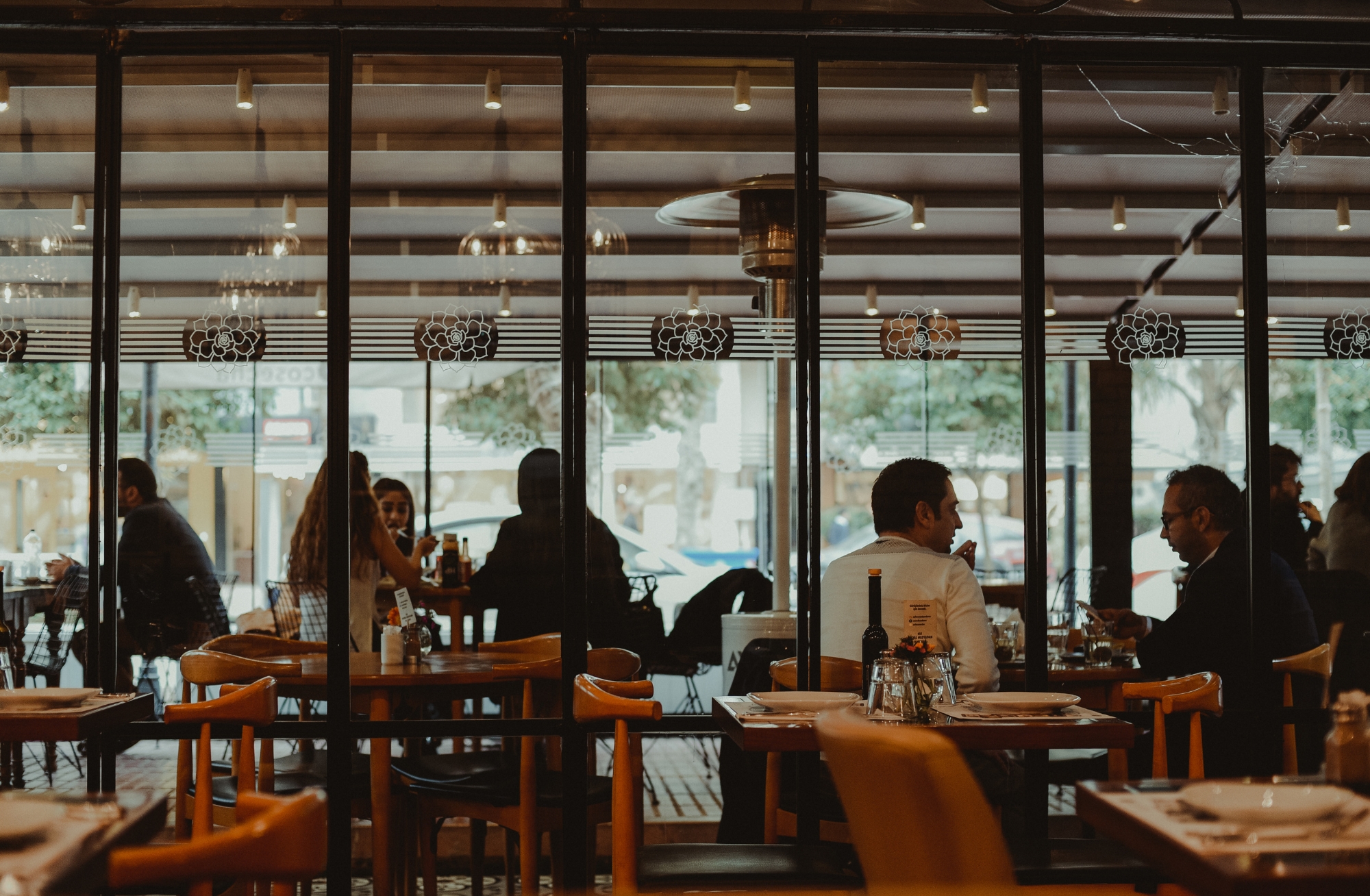 A photo taken of a restaurant from the outside window. People are sitting at tables and talking amongst themselves.