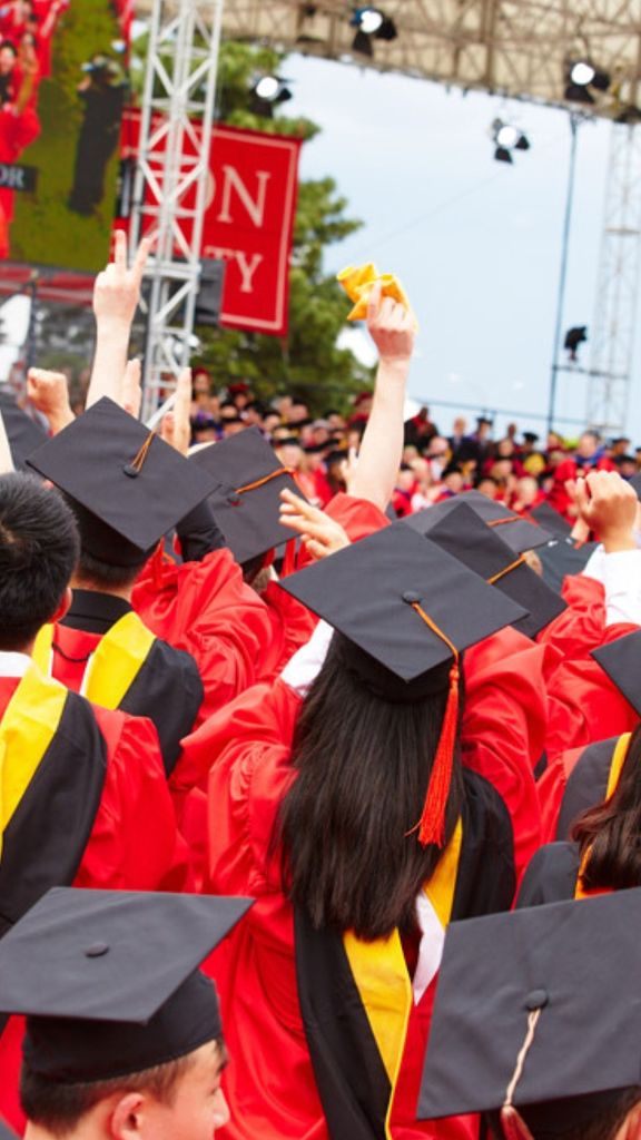 Boston University students in their caps and gowns, looking up at the stage at Commencement on Nickerson Field.