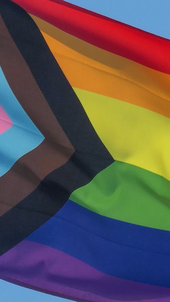 Photo: A picture of a pride flag being raised in front of a blue sky
