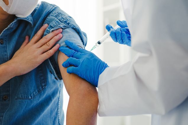 Photo: A person receiving an immunization shot from a doctor wearing blue gloves