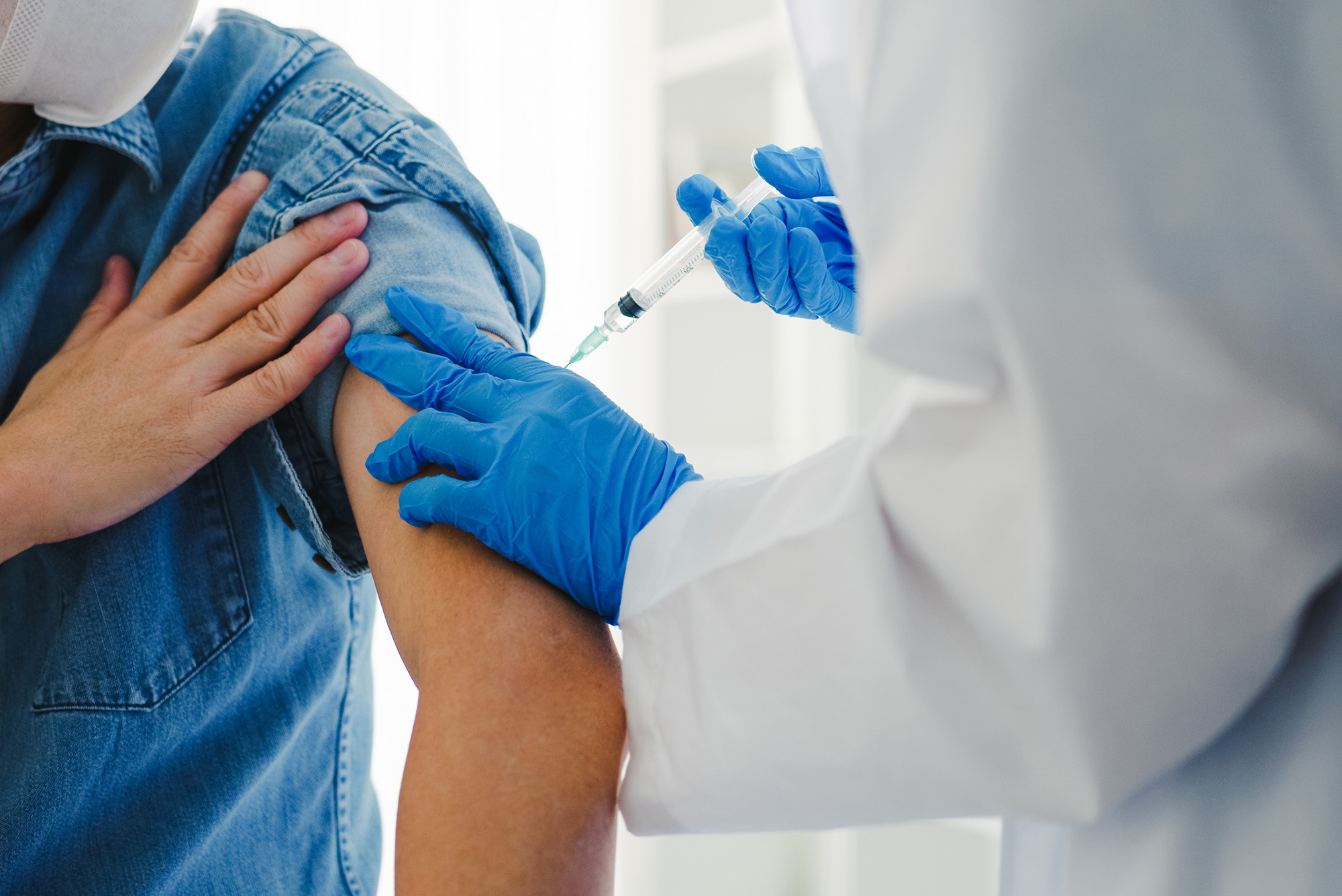 Photo: A person receiving an immunization shot from a doctor wearing blue gloves