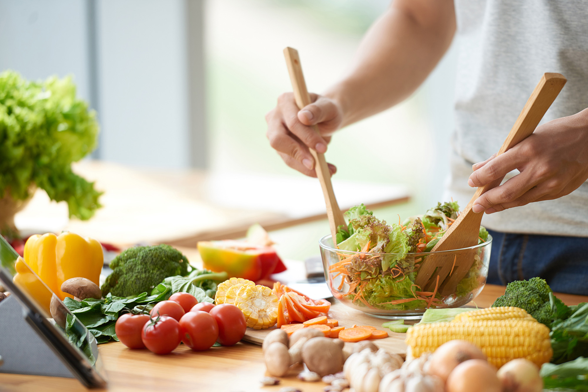 Photo: A man mixing a salad filled with green vegetables in a clear, glass bowl