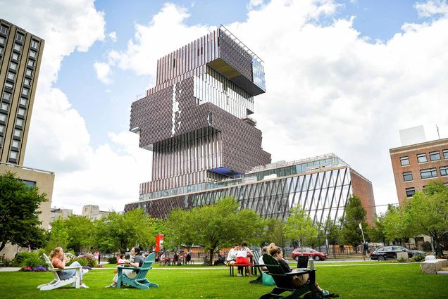 Photo: Boston University's COM Lawn filled with students on a sunny day. The Center for Computing and Data Sciences on Boston University's campus is visible in the background