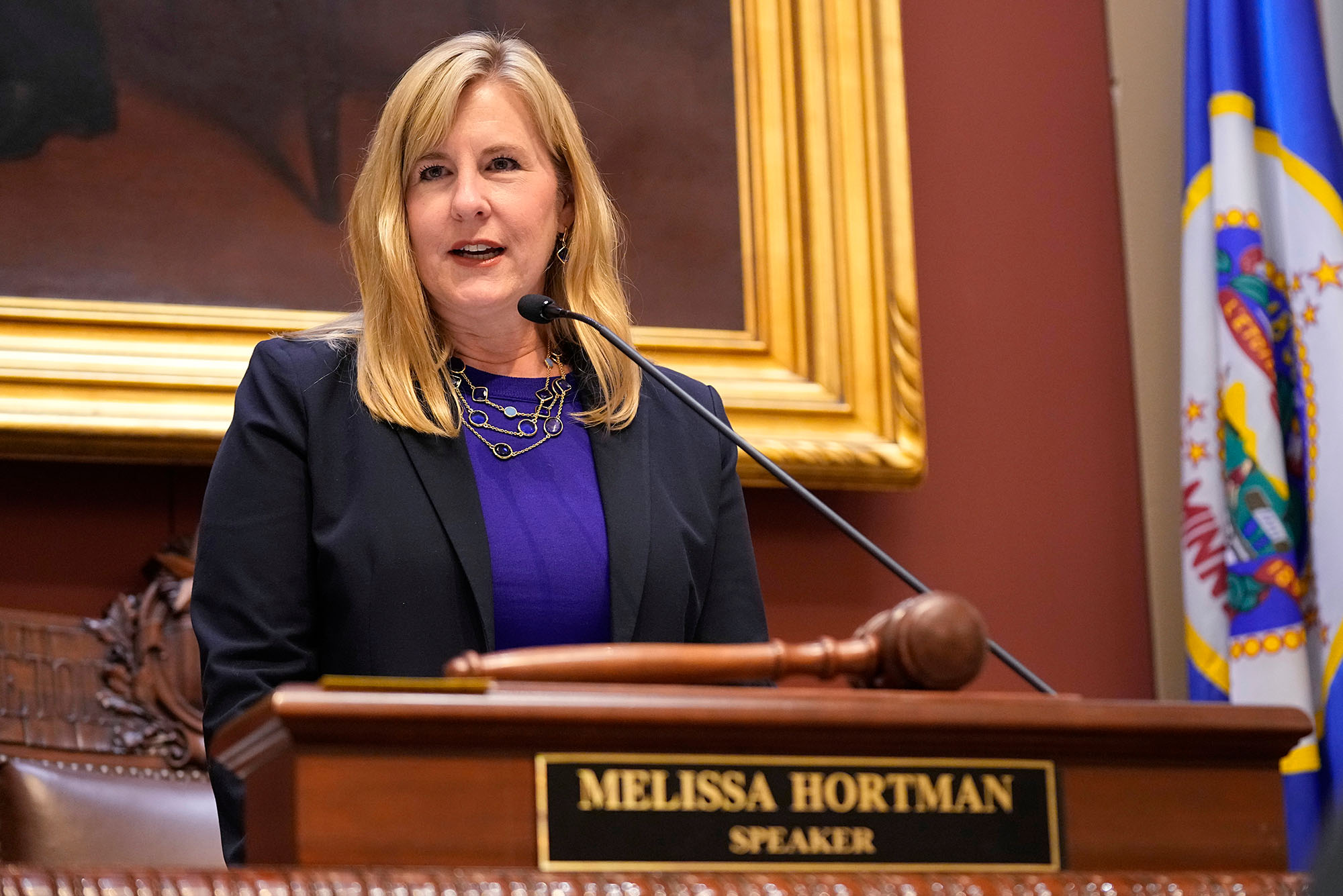 Photo: Melissa Hortman wearing a blazer and standing behind a podium that says "Melissa Hortman, Speaker"