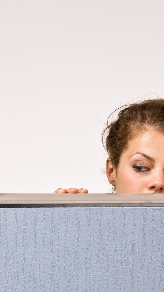 Photo: A businesswoman peering over cubicle wall
